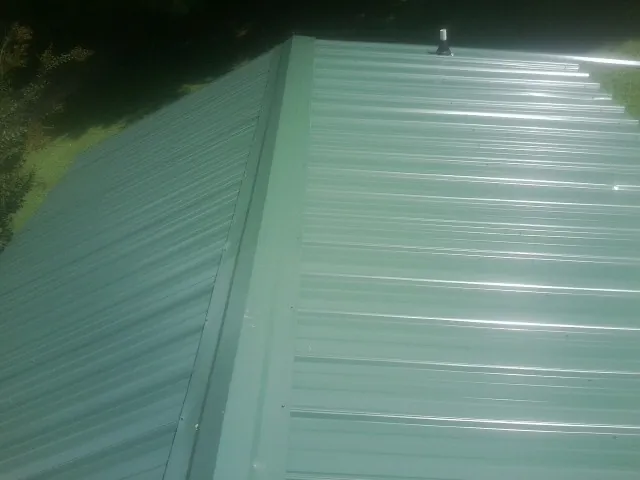New green metal panels meeting at the ridge of a roof — Flat Roof Repair work by our crew in Gardner