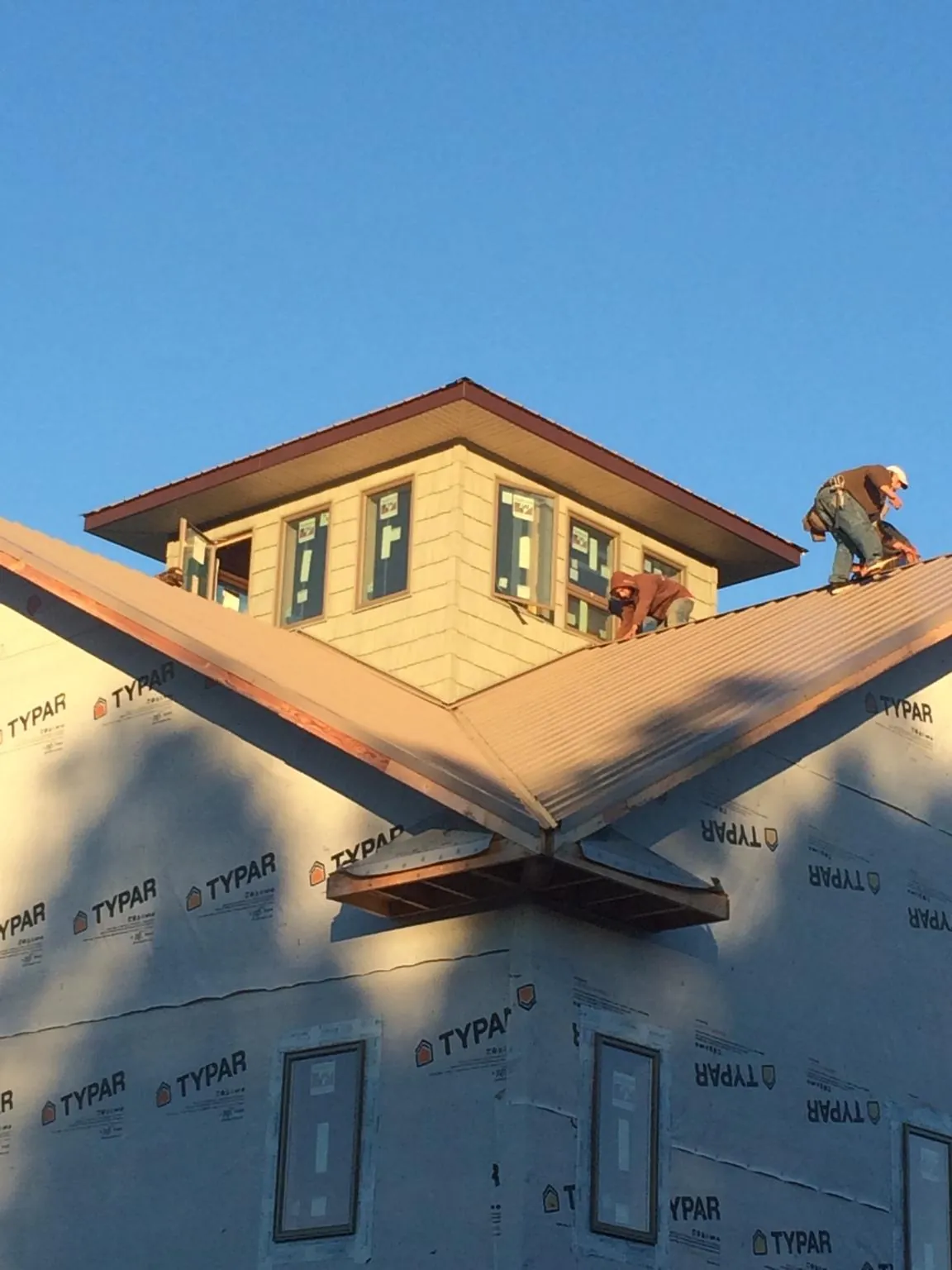 Roofers working around a rooftop cupola on a new metal roof at sunset in Gardner